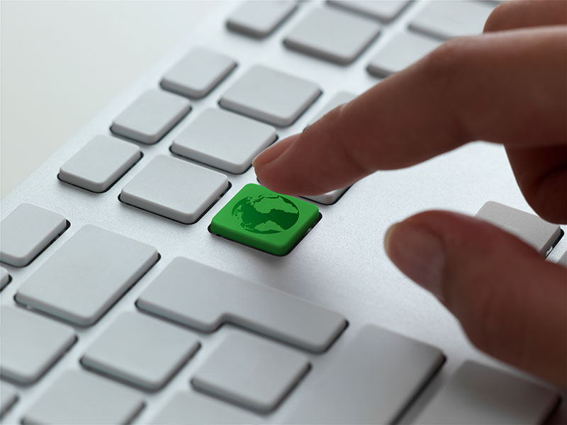 A finger pressing a green globe key on a keyboard