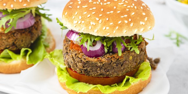 Two burgers are displayed on a white platter, each burger is made with a plant based protein patty, lettuce, onions, tomato, and a protein enriched bun