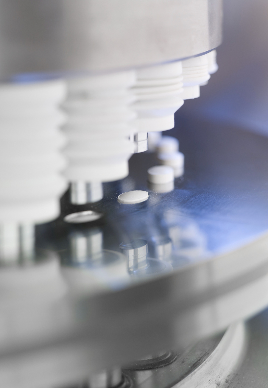 A tablet press used in pharmaceutical formulation development produces a line of white tablets.